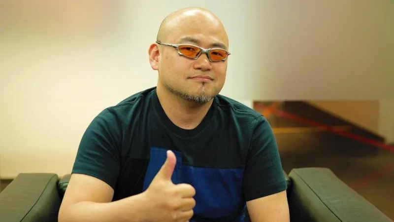 Hideki Kamiya speaking at a gaming event, with PlatinumGames’ logo displayed on a screen behind him.